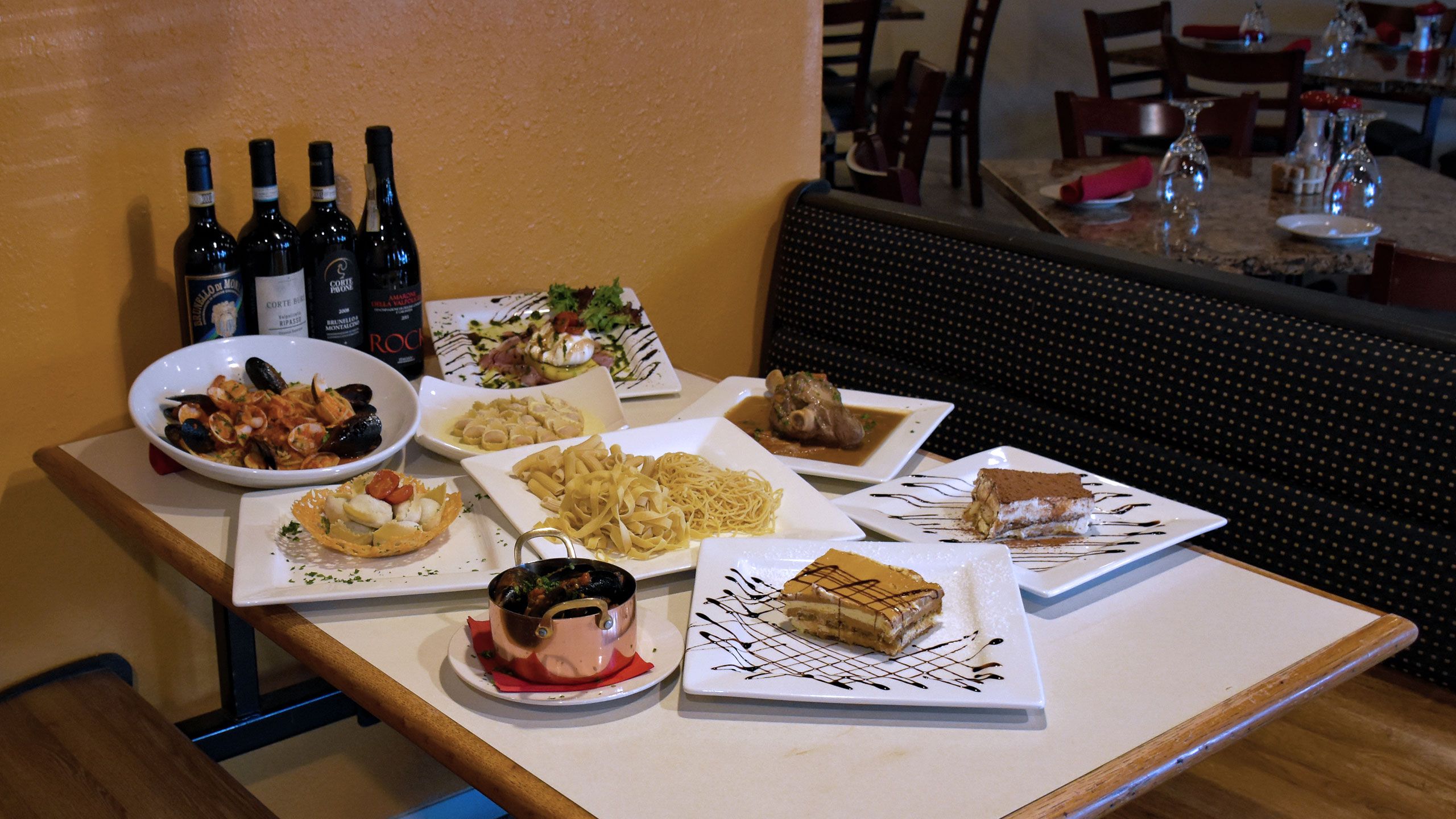 Bottles of wine and plates of homemade Italian food on a table at Tiramisu Ristorante Italiano.